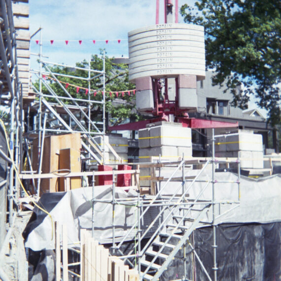 Photo of a construction site. There are steps made of metal scaffolding and various cinder blocks stacked on top of one another. There are red bunting flags hanging above the construction site.