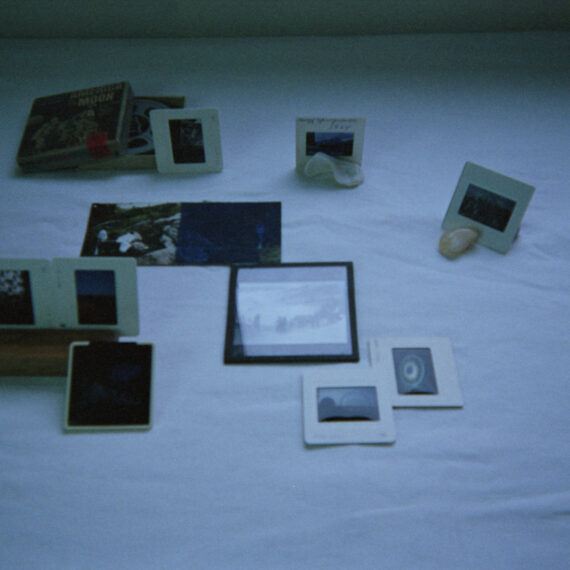 A collection of film slides are arranged on a white cloth. Some slides are propped up by small stones while others lay flat on the white cloth.