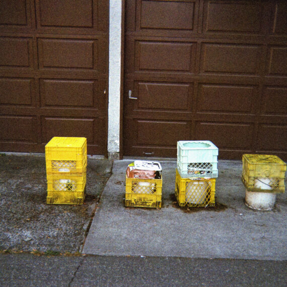 A row of milk crates draped over buckets on the asphalt in front of a brown garage door.