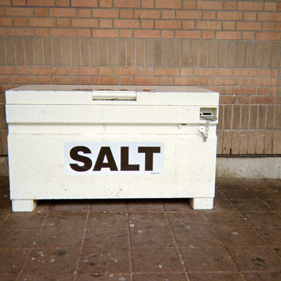 Photo of a white crate that is locked resting against a brick wall. The crate is labelled with black text that reads "SALT".