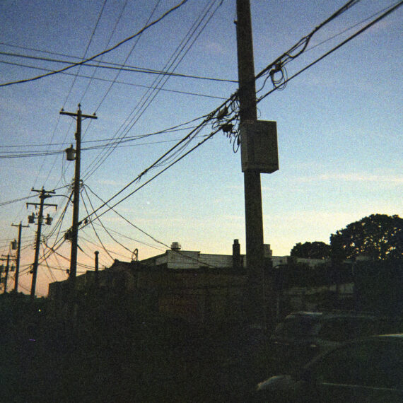 Photo of a row of power line silhouettes in an alley way. In the background is a blue and orange sky amidst a sunset.