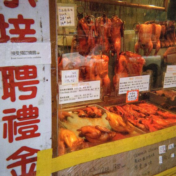 Colour photo of a window front of a Chinese barbecue meats store. There are small signs taped to the window.