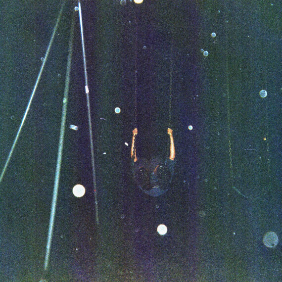 A photo of a person swinging on a swingset at night. The photo is underexposed with spot of white light scattered across the frame. The person on the swing is in mid-swing.