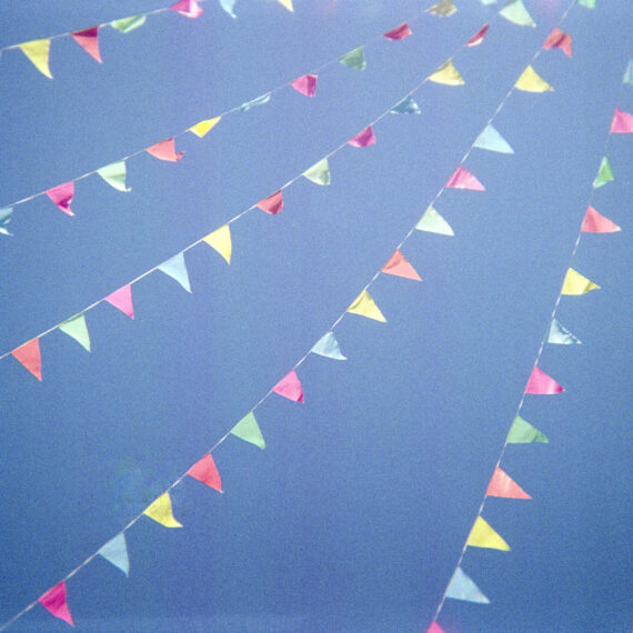 Photo of colourful bunting flags flapping in the wind. The bunting flags are dancing against a blue sky.