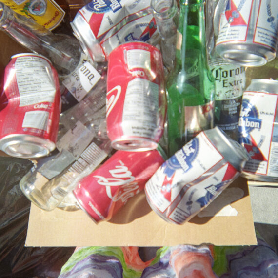 A box full of empty cans and bottles. There are a mixture of beer cans, soda cans, and beer bottles in the box.